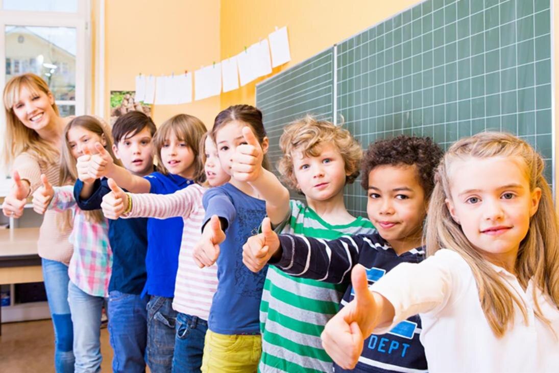 Acht kInder und eine Lehrerin lächeln in die Kamera und zeigen den Daumen nach oben