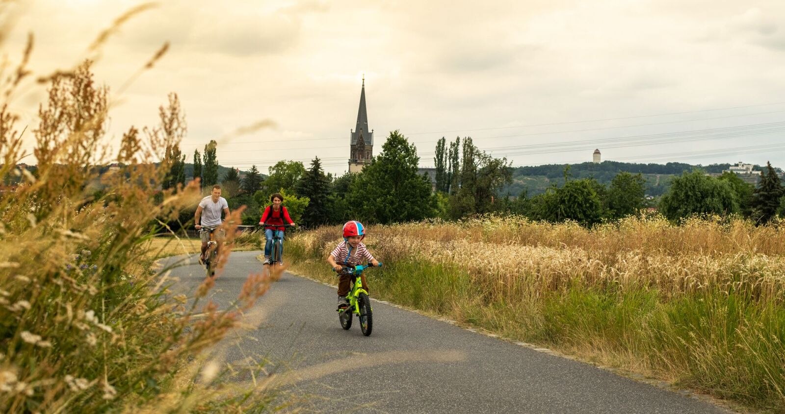 Eine Frau und ein Mann fahren mit ihrem Kind auf einem Radweg mit dem Fahrrad an einem Feld